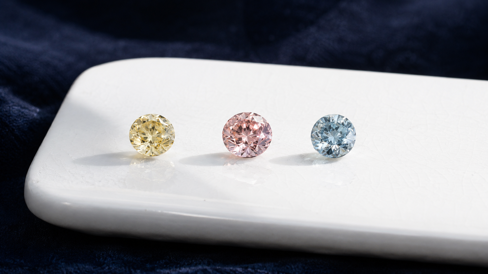 Three small diamonds in yellow, pink and pale blue arranged on a white ceramic tile under diffused daylight