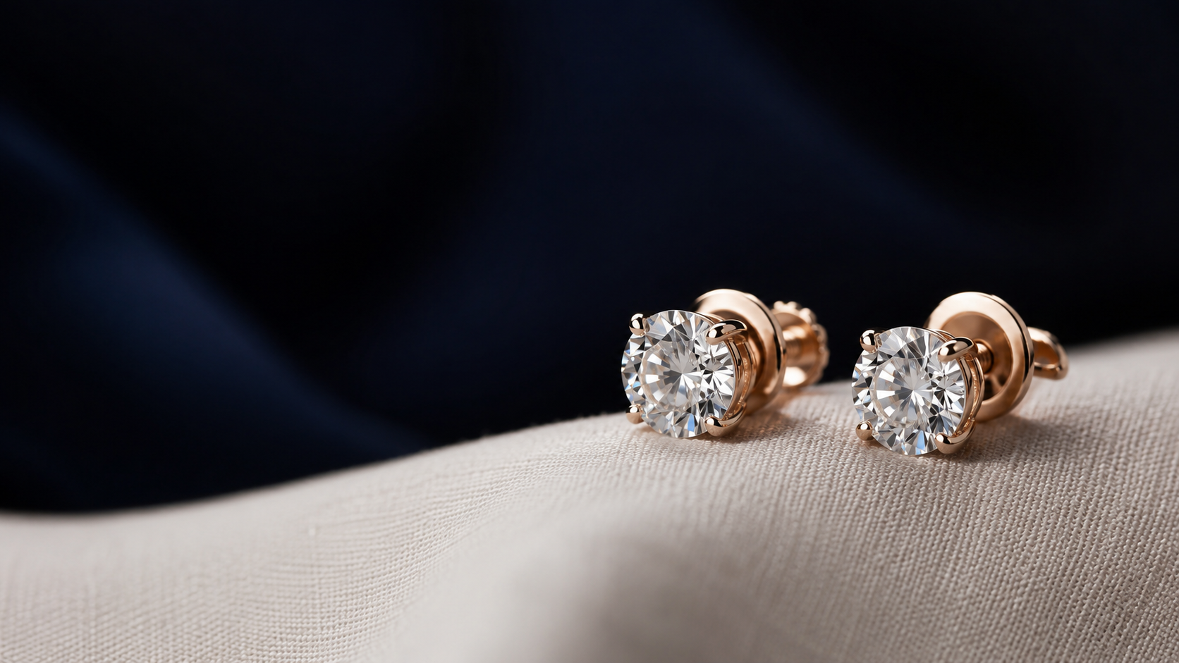 A pair of round diamond stud earrings with screw backs on a pale linen cloth