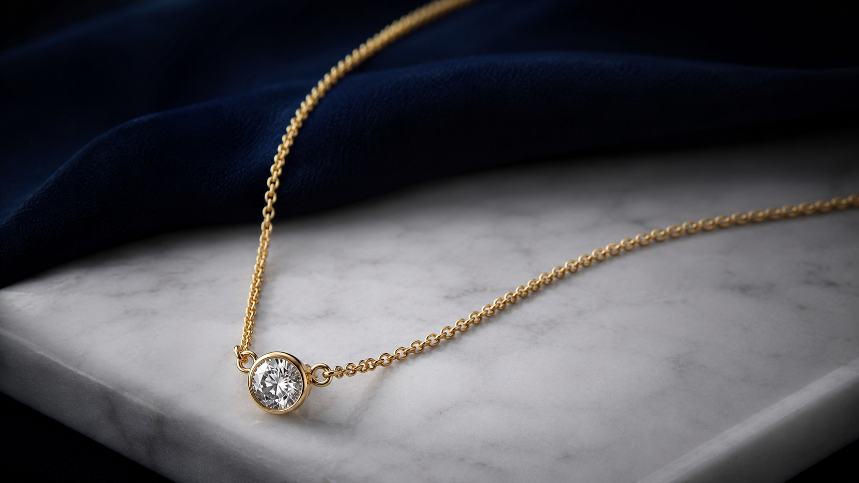 A round diamond pendant on a fine gold chain laid in a curve on white marble